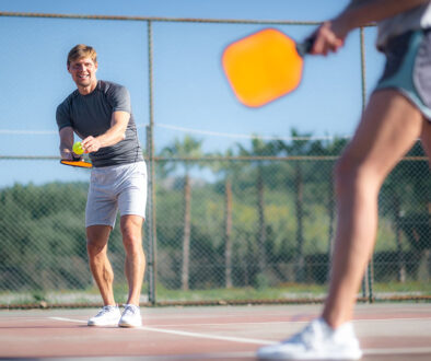 A Man Smiling While Serving A Pickleball To A Woman Wondering If He Needs Orthopedic Sports Medicine