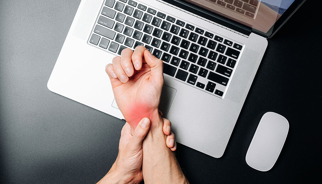 Man Holding His Wrist In Pain Above His Laptop Ultrasound Guided Carpal Tunnel Release