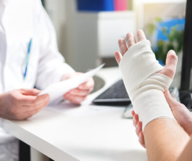 A Patient Holding a Bandaged Broken Hand on Their Doctor’s Desk Signs a Broken Bone Is Not Healing