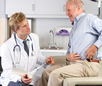 A Senior Male Patient Sitting Down Showing a Young Male Doctor Where He Is Experiencing Hip Pain How Long Does a Hip Replacement Last