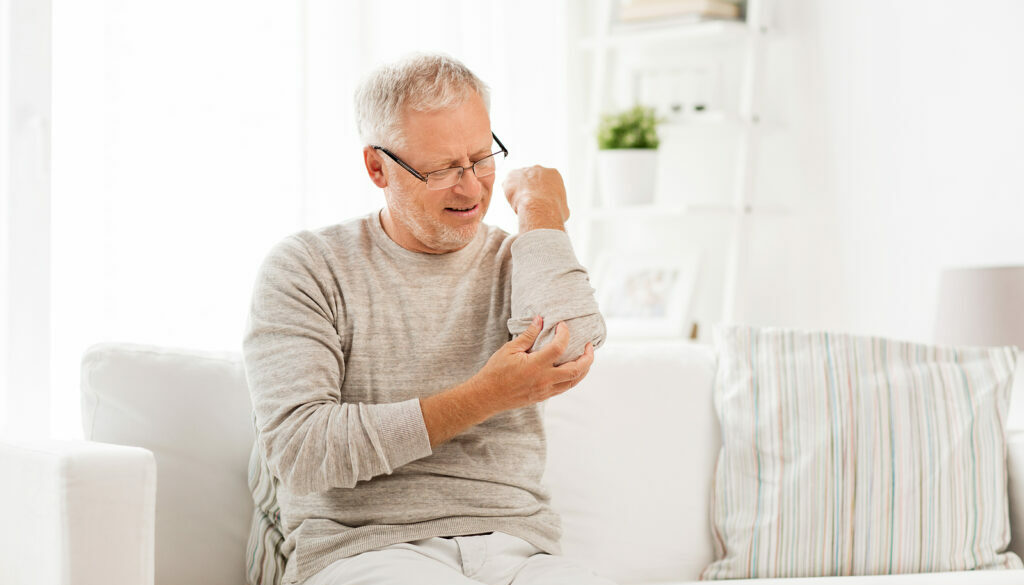 A Senior Man Sitting on a Couch Holding His Elbow in Pain Elbow Pain