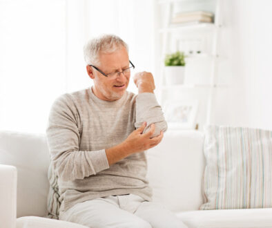 A Senior Man Sitting on a Couch Holding His Elbow in Pain Elbow Pain