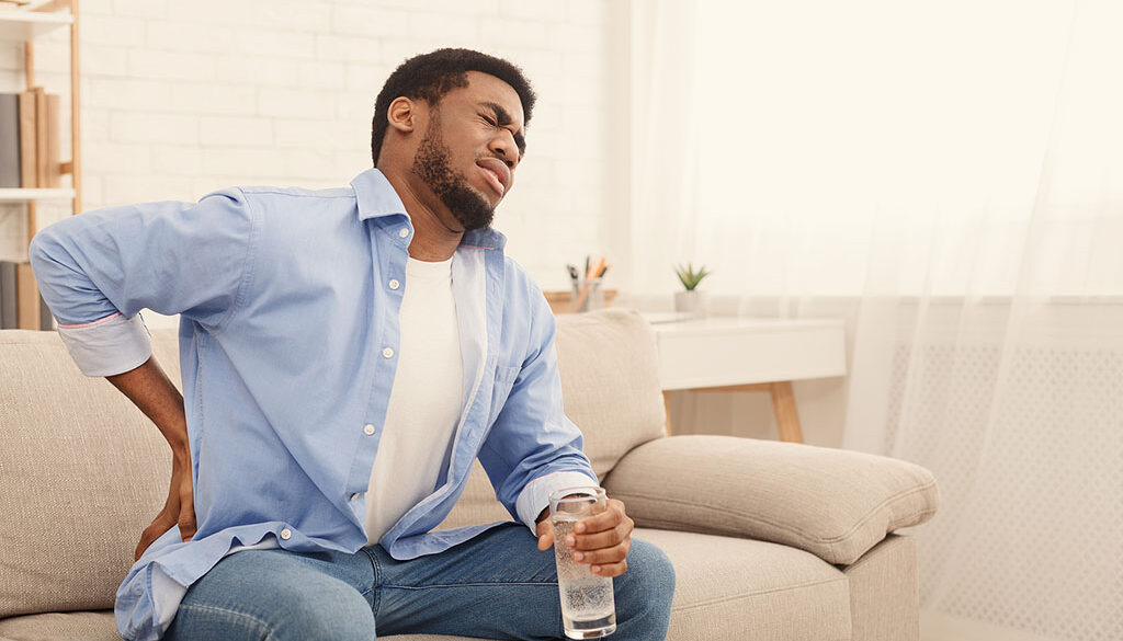 An African American Man Sitting on a Couch Holding His Hip in Pain Hip Impingement Syndrome