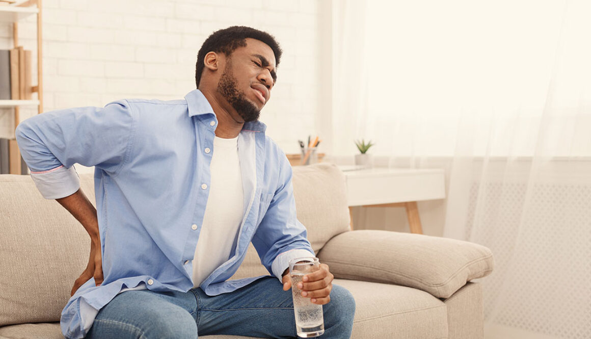 An African American Man Sitting on a Couch Holding His Hip in Pain Hip Impingement Syndrome