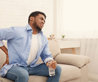 An African American Man Sitting on a Couch Holding His Hip in Pain Hip Impingement Syndrome