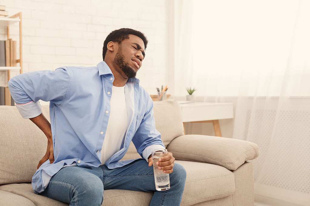 An African American Man Sitting on a Couch Holding His Hip in Pain Hip Impingement Syndrome