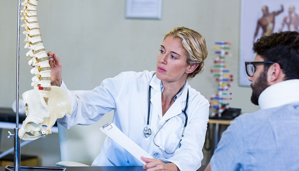 A Female Orthopedic Doctor Pointing to Spinal Discs on an Anatomical Spine Explaining the Benefits of Spinal Decompression Therapy to a Patient