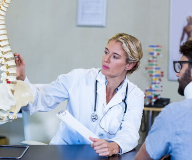 A Female Orthopedic Doctor Pointing to Spinal Discs on an Anatomical Spine Explaining the Benefits of Spinal Decompression Therapy to a Patient