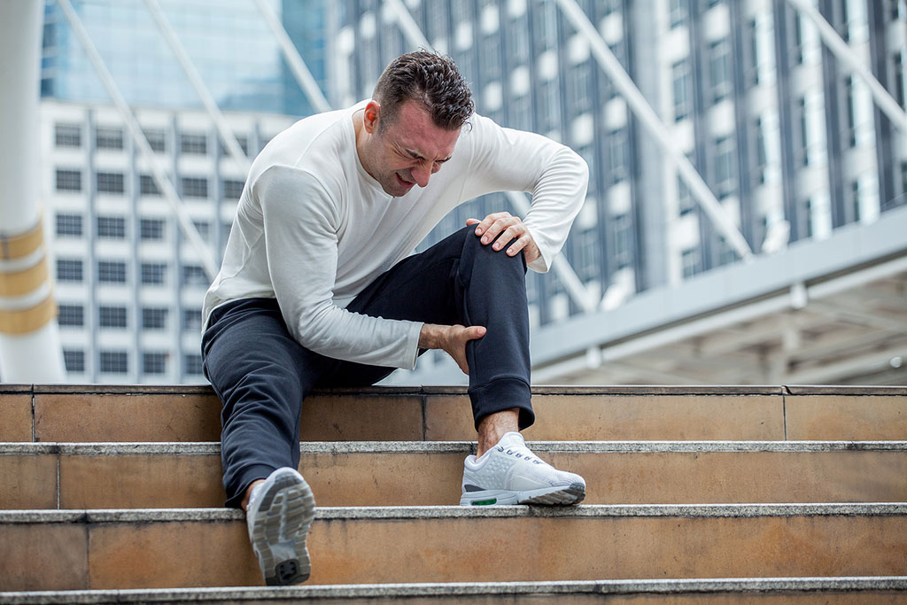 A Man Sitting on Stairs Holding His Calf in Pain Ruptured Achilles vs Torn Achilles