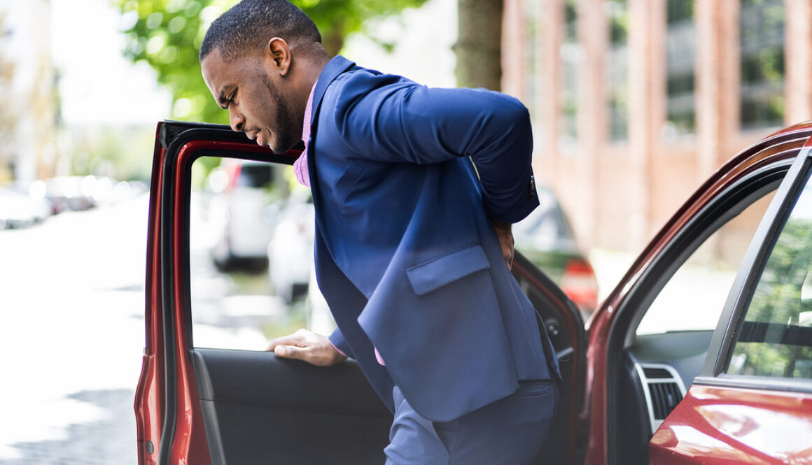 An African American Man Stepping Out Of A Car Holding His Lower Back Experiencing Back Pain After A Car Accident