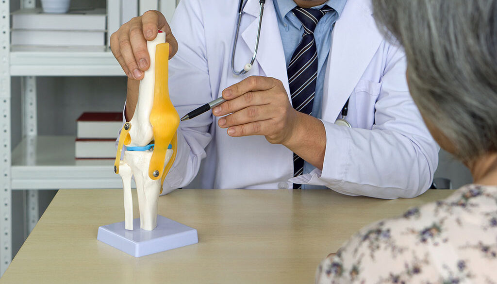 Closeup of a Board-Certified Orthopedic Doctor Pointing to a Model of a Knee With a Patient