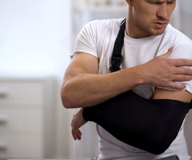 A Man Wearing His Arm In A Sling Reaching Towards His Shoulder With His Opposite Hand Frozen Shoulder After Surgery