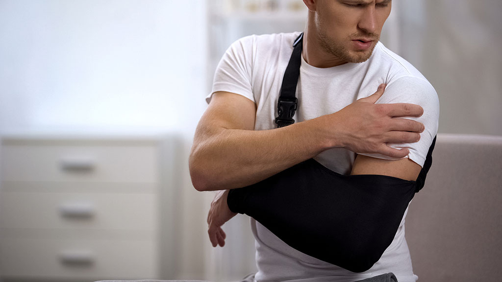 A Man Wearing His Arm In A Sling Reaching Towards His Shoulder With His Opposite Hand Frozen Shoulder After Surgery