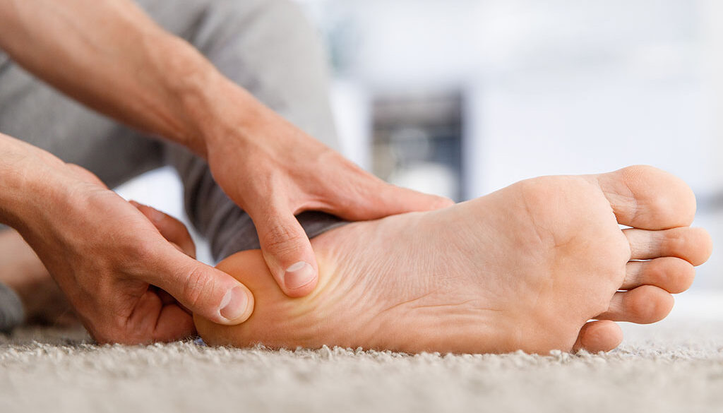 Closeup Of A Man Holding The Bottom Of His Foot In Pain From Heel Spurs